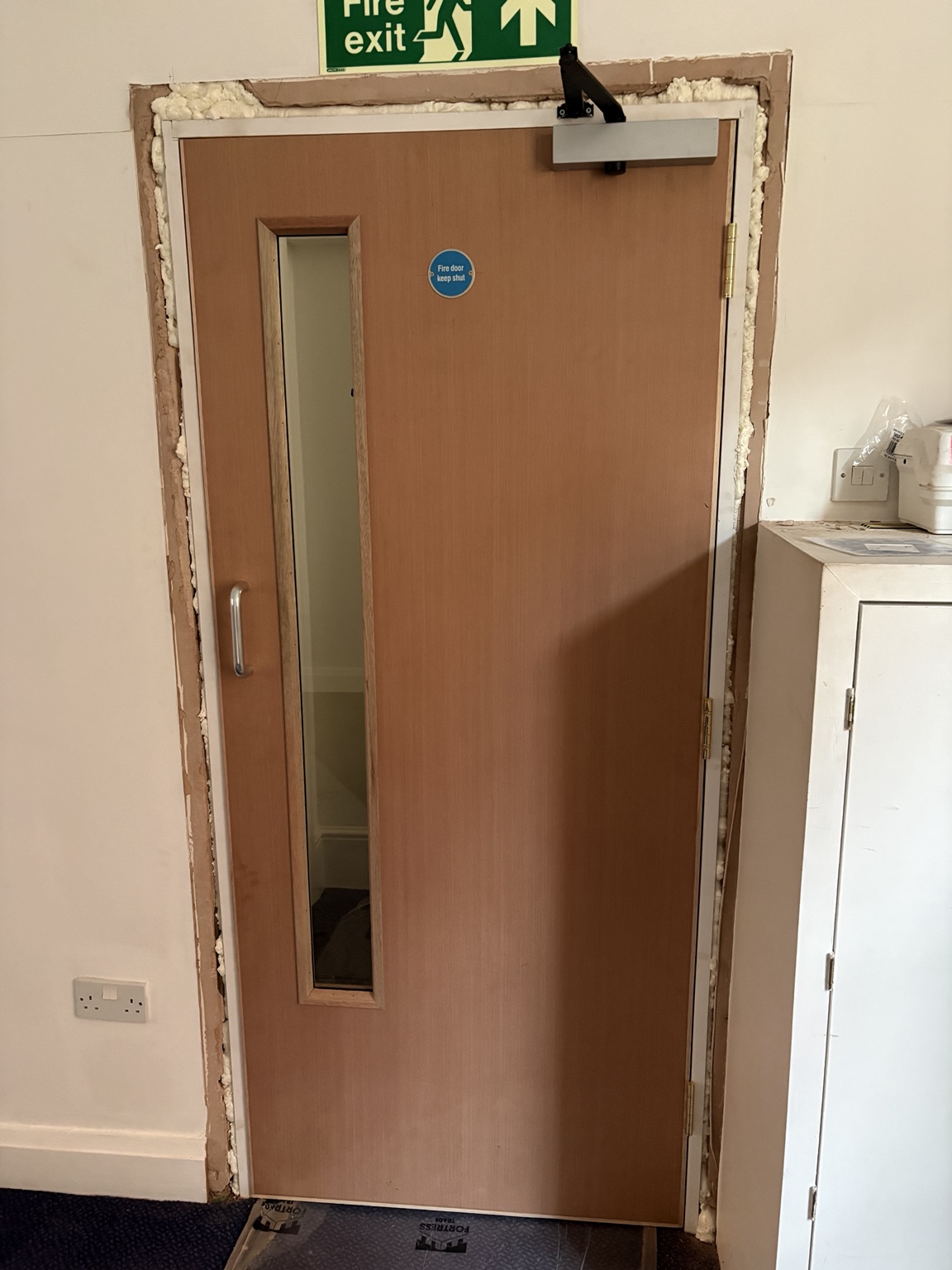 Newly fitted solid fire door with self-closing device during installation at a recent project, before final making good and decoration